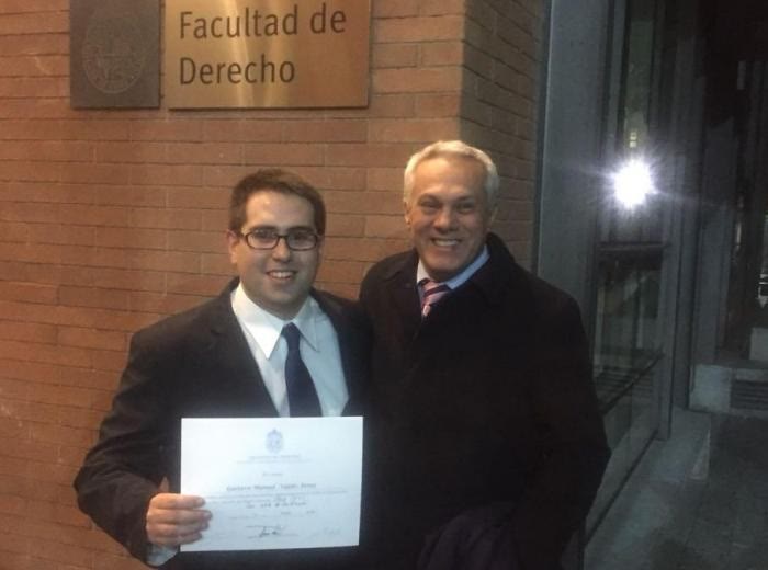 Un recién licenciado con su certificado junto a Guillermo Palacios, frente a la Facultad de Derecho